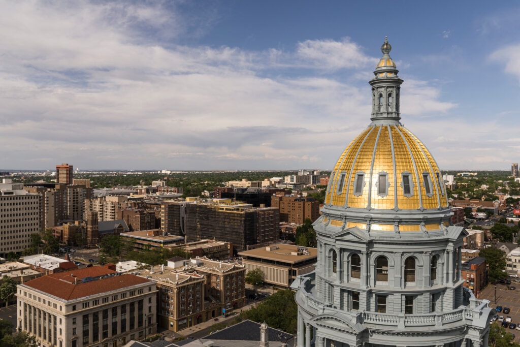 An aerial view of the gilded dome atop the Colorado Capitol in Denver. The city of Denver is seen behind it.