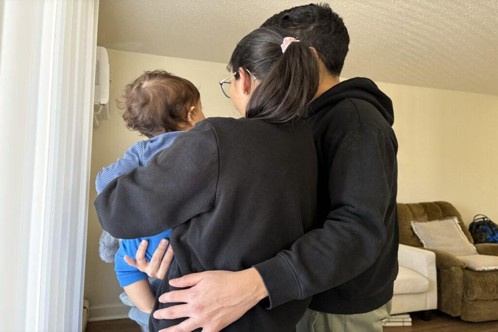 As ICE Moved In, Minnesotans Set Up a Shadow Medical System. It’s a Lesson for Other Cities. The back of a mother, father, and young baby being held by its mother. They are embracing.
