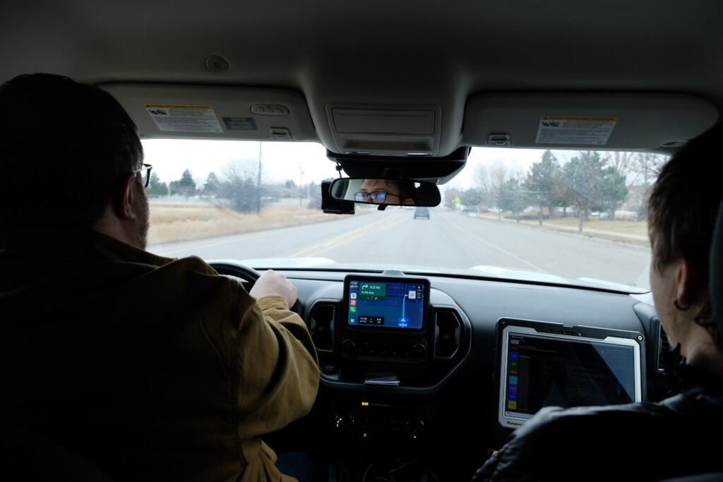 Despite Their Successes, Some Mobile Crisis Response Teams Are in Crisis A photo from the back seat of a car, two men in the front and passenger seat driving