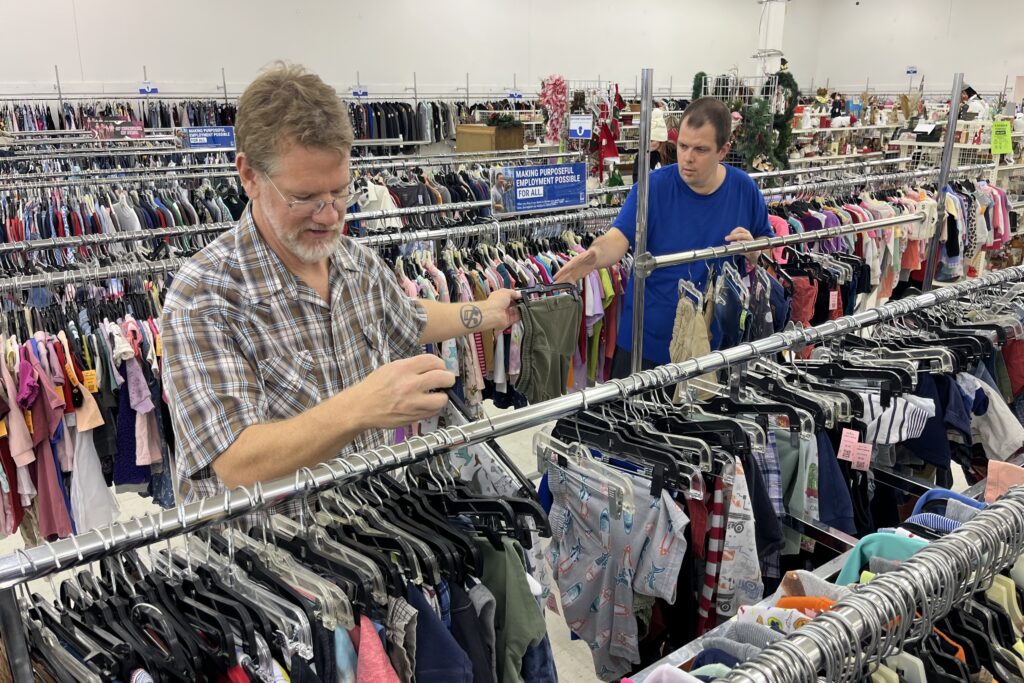 Trump’s Cuts to Medicaid Threaten Services That Help Disabled People Live at Home Two men sort racks of clothes in a Goodwill store.