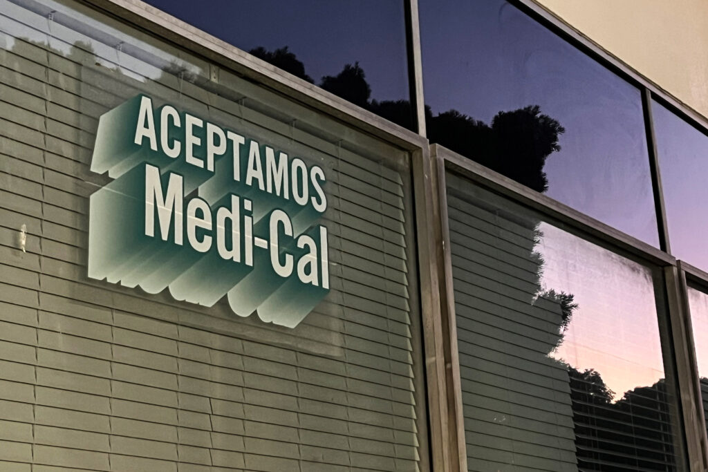 Medi-Cal Immigrant Enrollment Is Dropping. Researchers Point to Trump’s Policies. A sign printed on a window reads "Aceptamos Medi-Cal."