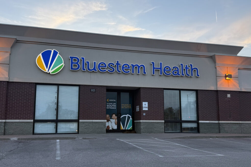 An exterior of a health clinic with a blue sign that reads, "Bluestem Health."